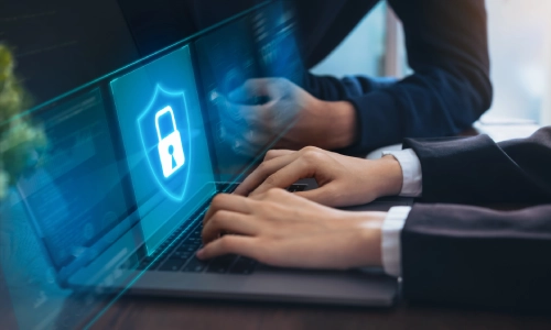 Two people working on a laptop with a holographic digital shield and lock icon representing cybersecurity and data protection.
